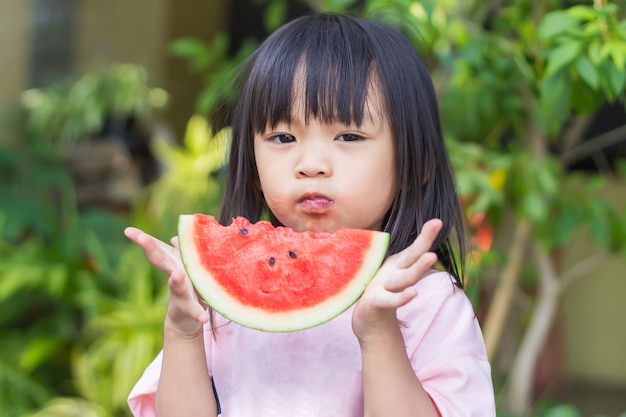 Foto menina feliz criança asiática comendo e mordendo um pedaço de melancia.