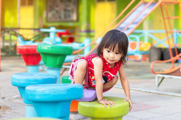 Menina feliz criança asiática escalando e jogando o brinquedo no parque infantil.