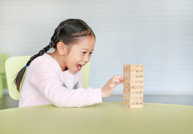 Menina feliz criança asiática jogando blocos de madeira torre jogo de habilidade de desenvolvimento cerebral e físico em uma sala de aula. concentre-se no rosto de crianças. garoto imaginação e conceito de aprendizagem.