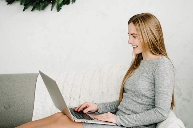 Menina feliz cumprimentando amigos ou família com ano novo em bate-papo por vídeo no laptop Jovem mulher usando laptop no escritório doméstico perto de pinheiro decorado em casa com interior de Natal com espaço de cópia