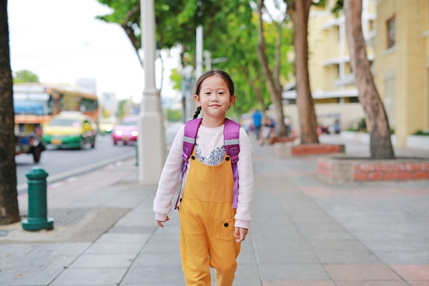 Menina feliz da criança asiática que anda com o schoolbag do ombro do estudante.