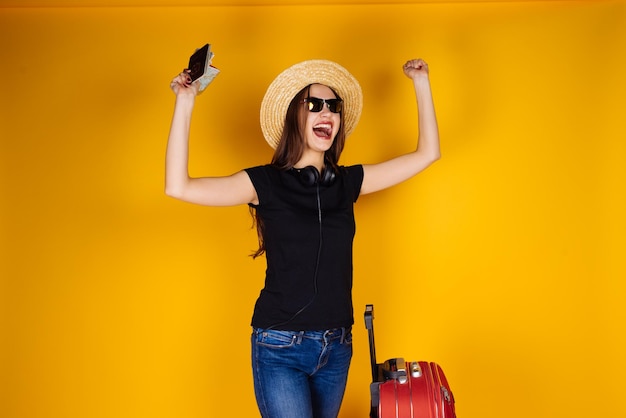 Menina feliz de chapéu e óculos sai de férias com uma grande mala vermelha no avião