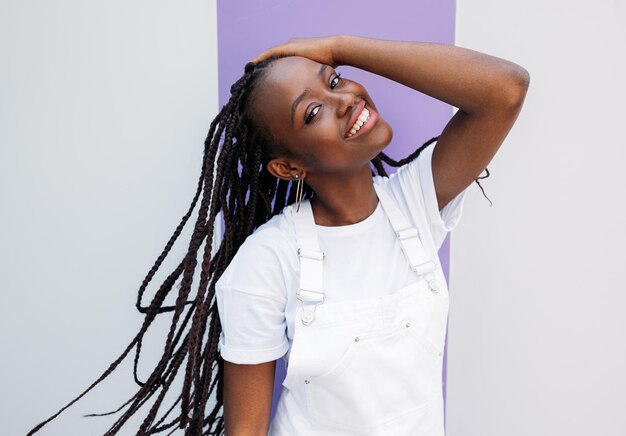 Foto menina feliz de uniforme branco ajustando suas tranças longas e olhando diretamente para uma câmera