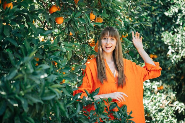 Menina feliz de vestido laranja está posando para a câmera segurando as mãos no jardim laranja