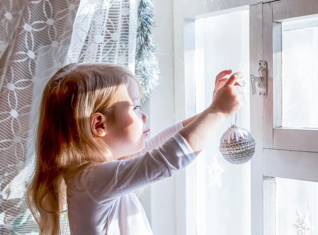 Menina feliz decora a janela com decorações de Natal, antecipação do Natal, ano novo