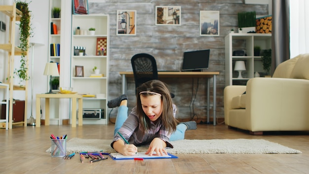 Foto menina feliz deitada no chão na sala de estar de desenho. garoto inteligente.