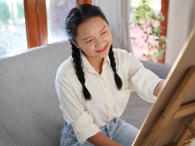 Menina feliz desenhando com uma paleta de pintura e um pincel em casa, pintando um artista