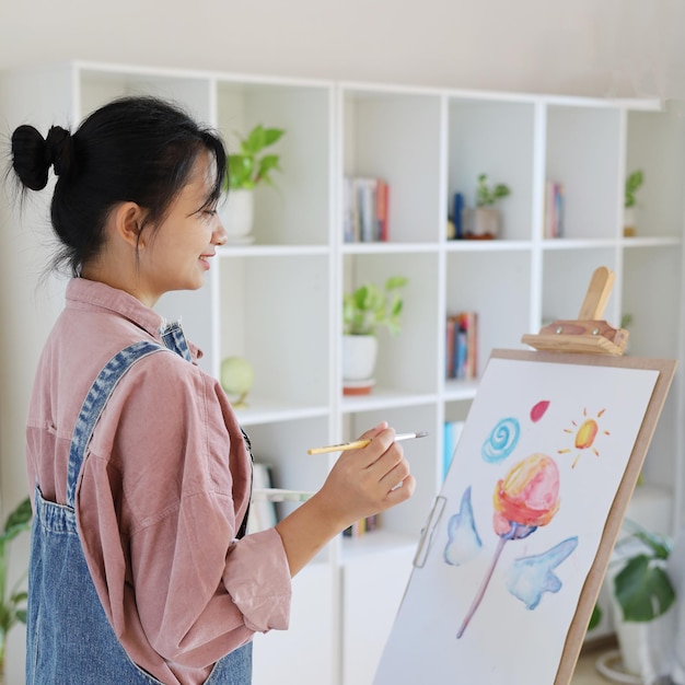 Menina feliz desenhando com uma paleta de pintura e um pincel no artista de pintura em casa