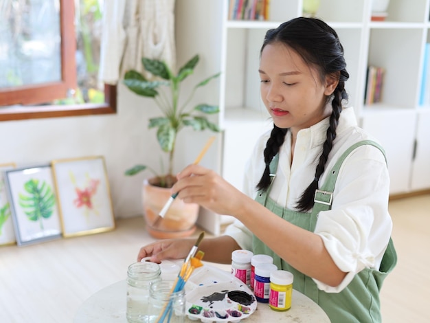 Menina feliz desenhando com uma paleta de pintura e um pincel no artista de pintura em casa