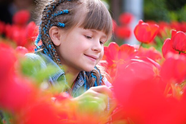 Menina feliz desfrutando do cheiro doce de flores de tulipas vermelhas no jardim de verão