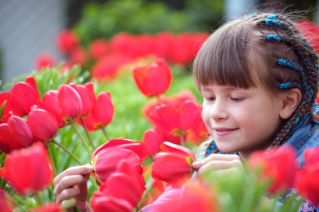 Menina feliz desfrutando do cheiro doce de flores de tulipas vermelhas no jardim de verão