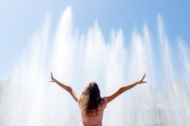 Menina feliz dia de sol e mãos para cima com a fonte, sentindo a liberdade