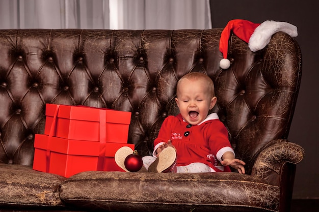 Menina feliz disfarçada de Papai Noel sentada no velho sofá na árvore de Natal decorada rindo