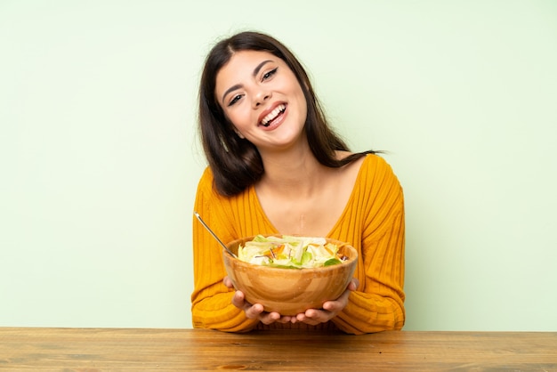 Menina feliz do adolescente com salada sobre a parede verde