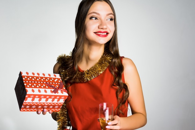 Menina feliz e sorridente com vestido vermelho comemorando o ano novo, segurando um presente e uma taça de champanhe