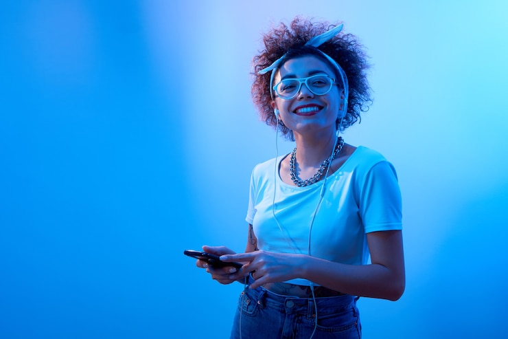 Foto menina feliz e sorridente na moda com cachos afro ouve e gosta de música com fones de ouvido, modelo estilo hip hop com smartphone relaxa