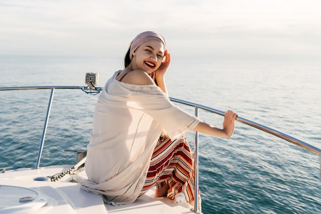 Foto menina feliz em calças de verão da moda desfruta de férias em seu iate nos raios do sol da noite