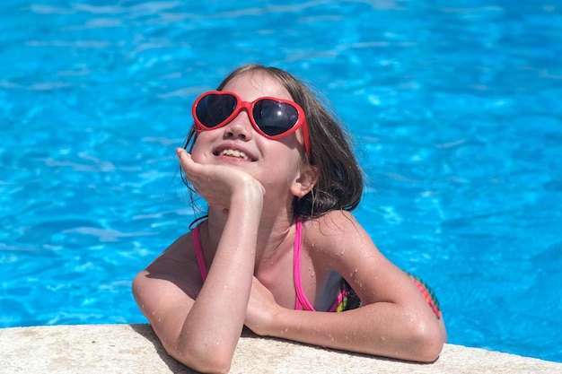 Menina feliz em óculos de sol na piscina em dia ensolarado Sonhos de infância e conceito de verão