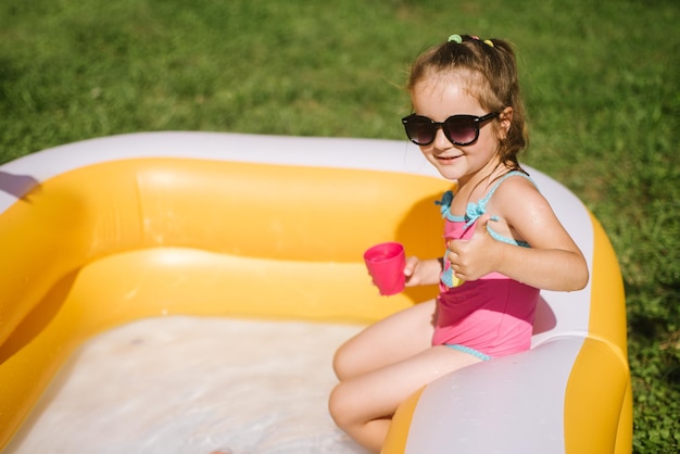 Menina feliz em traje de banho jogando na piscina inflável em dia ensolarado