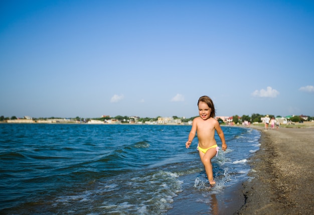 Menina feliz em trajes de banho correndo na praia