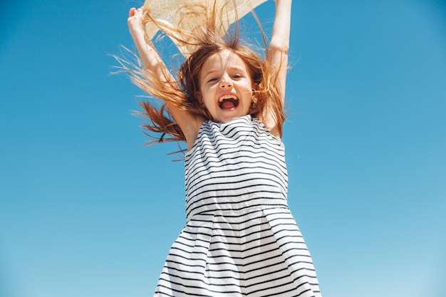 Menina feliz em um chapéu de palha pulando na praia nas férias de verão