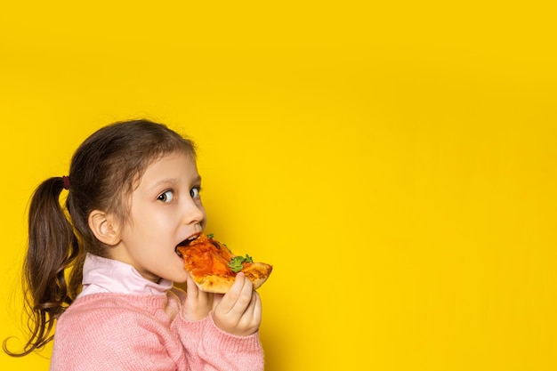 Menina feliz em um fundo amarelo. A criança está comendo pizza. pizza margarita. Garota legal e satisfeita.