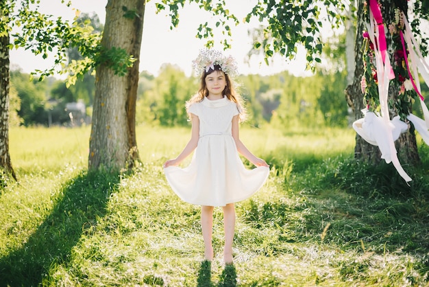 Menina feliz em um vestido com uma coroa de flores na cabeça de flores no campo