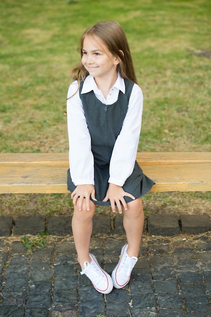 Menina feliz em uniforme escolar formal sentada no banco do parque colegial