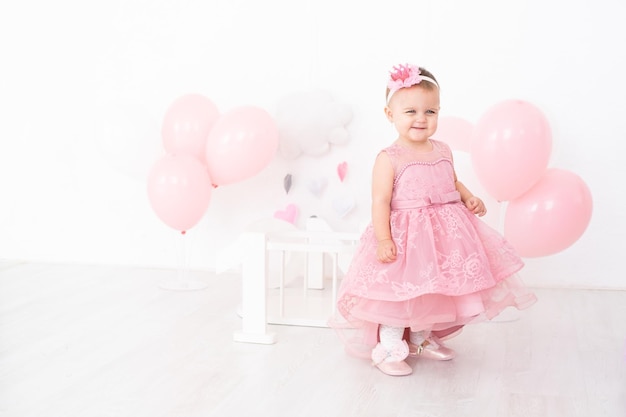 Menina feliz em vestido rosa comemorando seu primeiro aniversário com balões