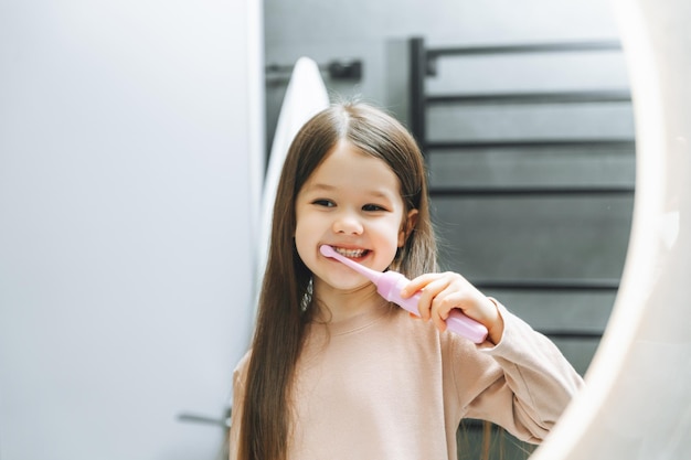 Menina feliz escovando os dentes na frente de um espelho de banheiro Higiene matinal