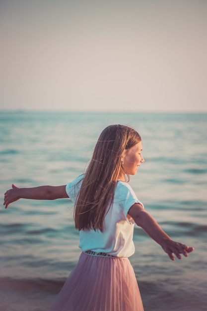 Foto menina feliz está girando e dançando na praia em um dia ensolarado.