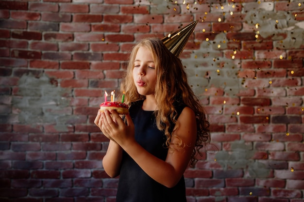 Menina feliz faz um pedido e sopra velas em um bolo no seu aniversário