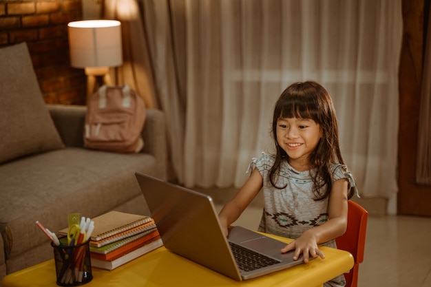 Menina feliz fazendo lição de casa usando laptop