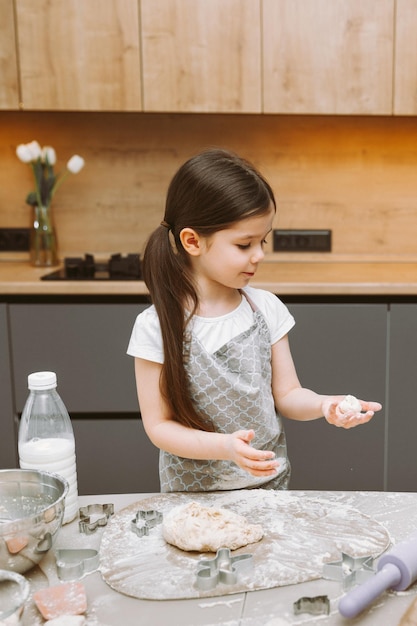 Menina feliz fazendo massa na cozinha uma criança pequena aprende a cozinhar ou assar massa de fermento com as mãos em casa