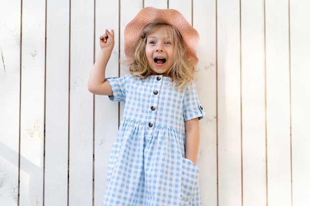 Foto menina feliz fica ao lado da parede de madeira branca e sorri