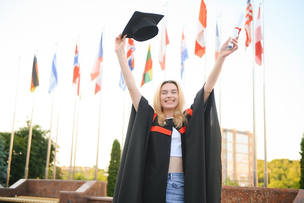 Foto menina feliz graduada na universidade a garota está parada perto da universidade no contexto das bandeiras de diferentes países o conceito de educação internacional