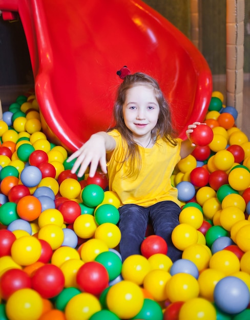 Menina feliz jogando e se divertindo no jardim de infância com bolas coloridas no play center