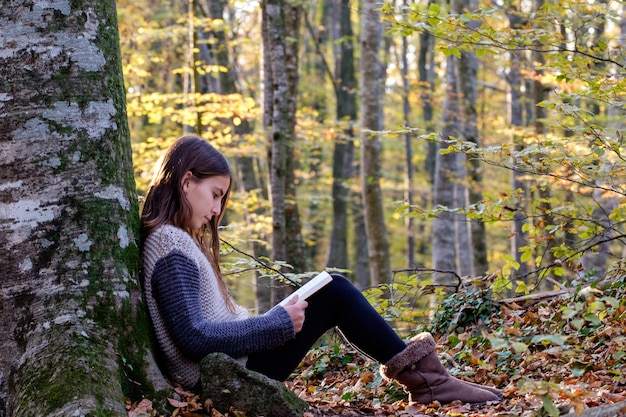 Menina feliz lendo um livro na floresta de outono