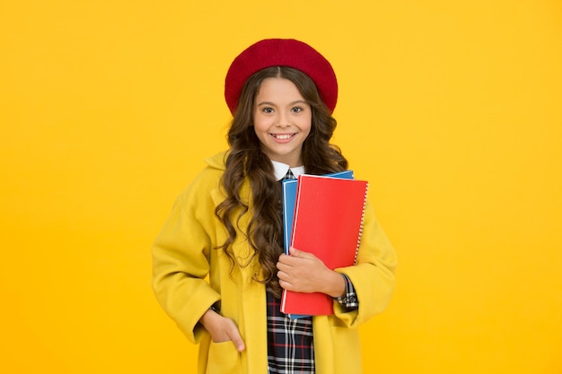 Menina feliz na boina segura a escola de cadernos