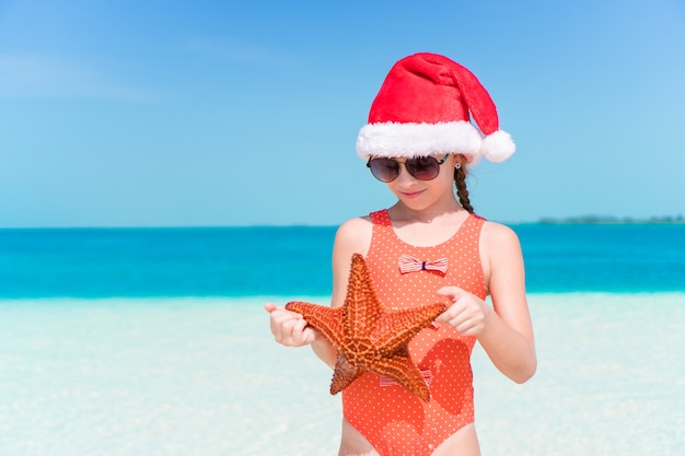 Menina feliz no chapéu de Papai Noel durante as férias de praia de Natal se divertir