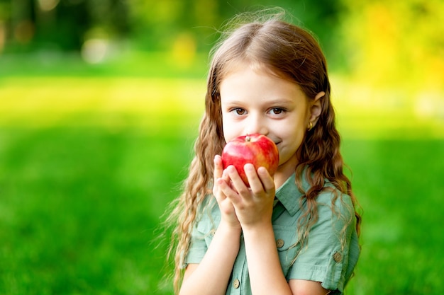 Menina feliz no verão no gramado com uma maçã vermelha na grama verde e espaço sorridente para texto