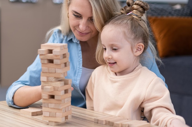 Menina feliz olhando para a torre jenga praticando lógica e gostando de jogar com a mãe