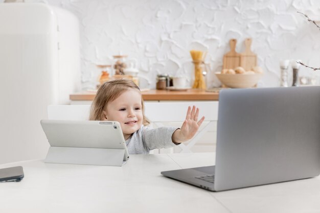 Menina feliz olhando para o laptop e dizer oi para seus amigos Garoto sentado em casa durante a quarentena