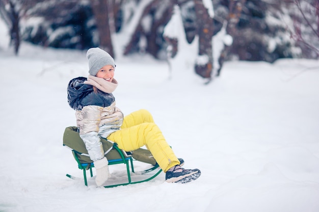 Menina feliz pequena adorável que sledding no dia nevado do inverno.