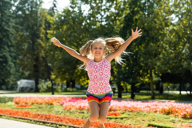 Menina feliz pulando no parque. menina tomando sorvete e se divertindo na cidade.