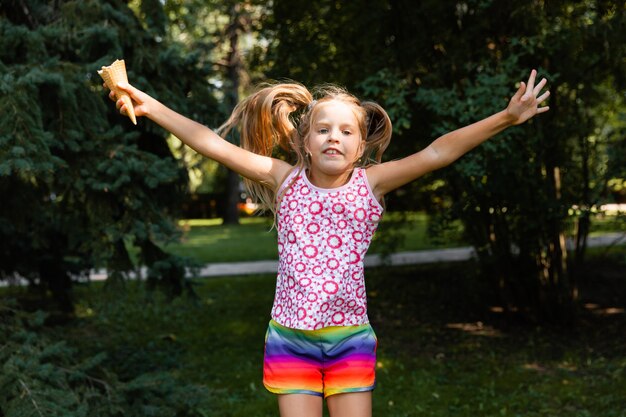 Foto menina feliz pulando no parque. menina tomando sorvete e se divertindo na cidade.