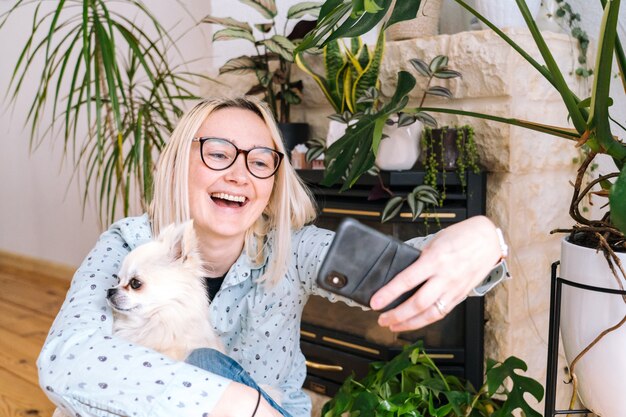 Menina feliz que senta em casa a cozinha e que guarda o videocall. jovem mulher usando smartphone para vídeo chamada com amigo ou família. webinar de gravação do vlogger. mulher olhando a câmera e acenando as mãos de saudação