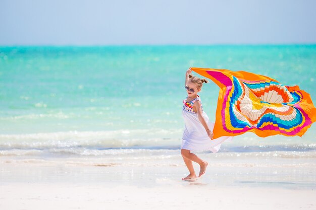 Menina feliz se divertindo correndo com pareo na praia tropical branca