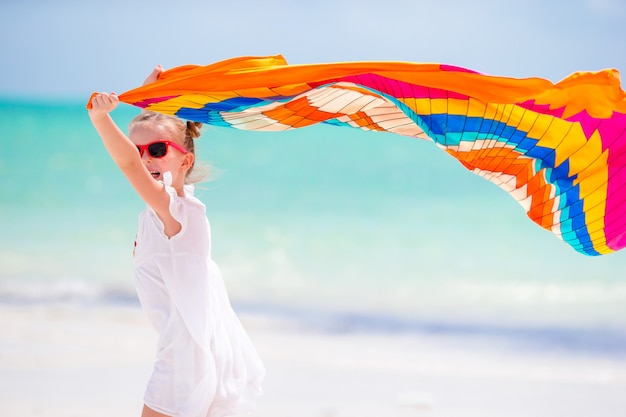 Menina feliz se divertindo correndo com pareo na praia tropical branca