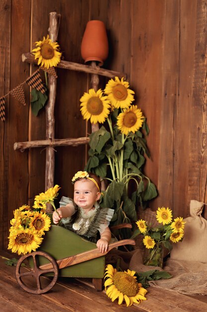 Menina feliz se divertindo e brincando entre os girassóis florescendo perto do carrinho